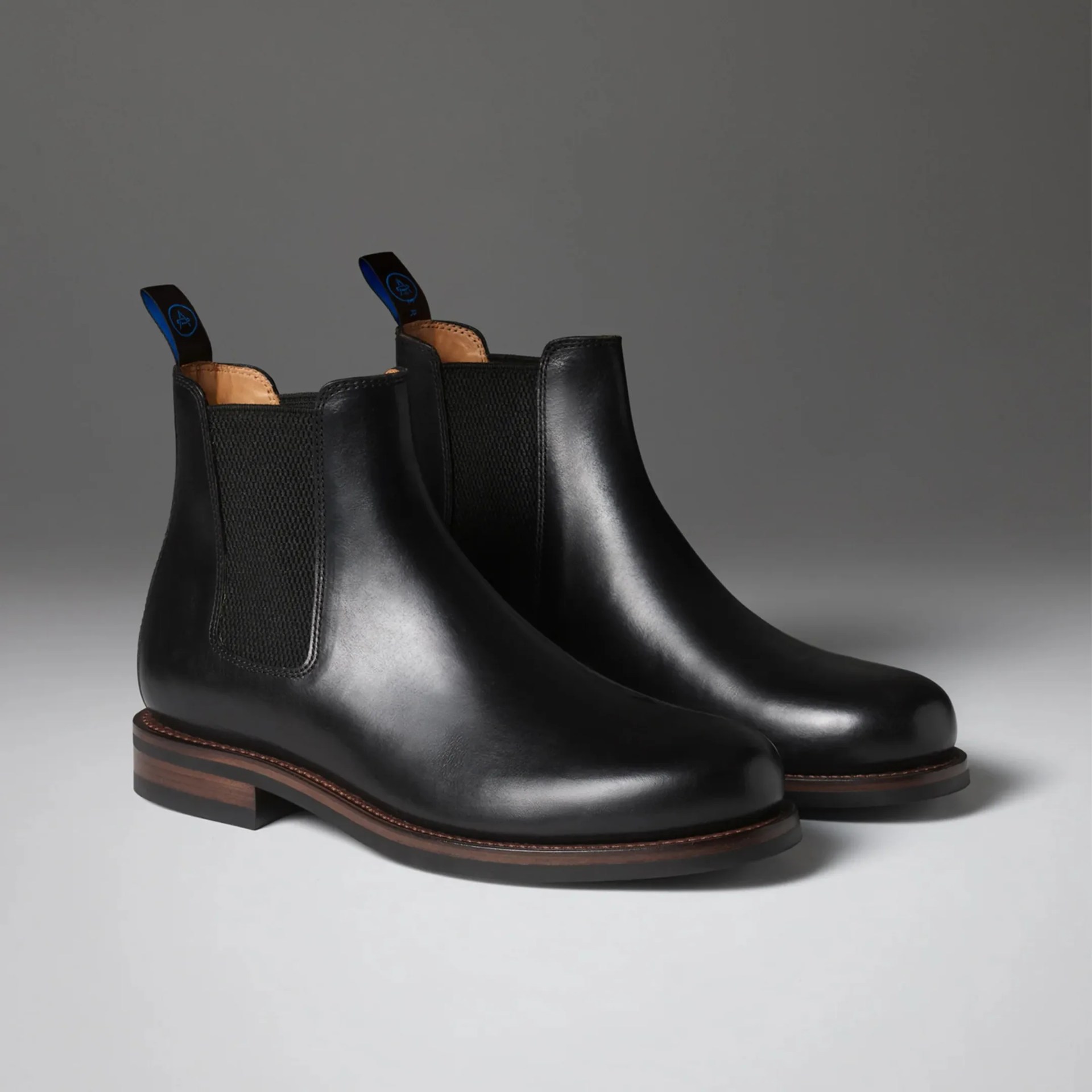 Pair of black leather Chelsea boots with elastic side panels and brown stacked heels on a gray surface.