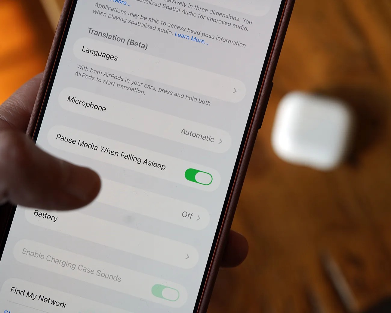Smartphone screen showing AirPods settings with "Pause Media When Falling Asleep" toggle enabled, AirPods case blurred in background.