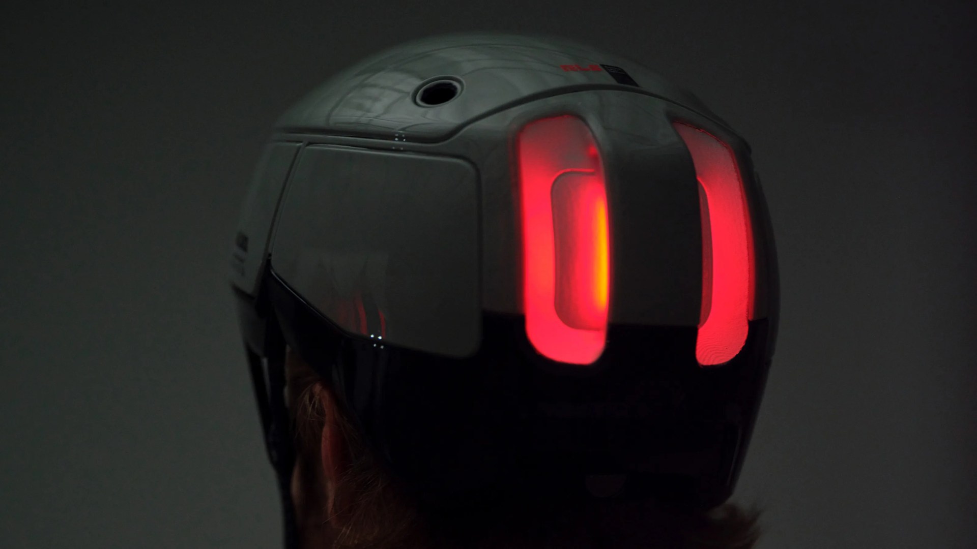 White and black bicycle helmet with two vertical red LED lights on the back, worn by a person.