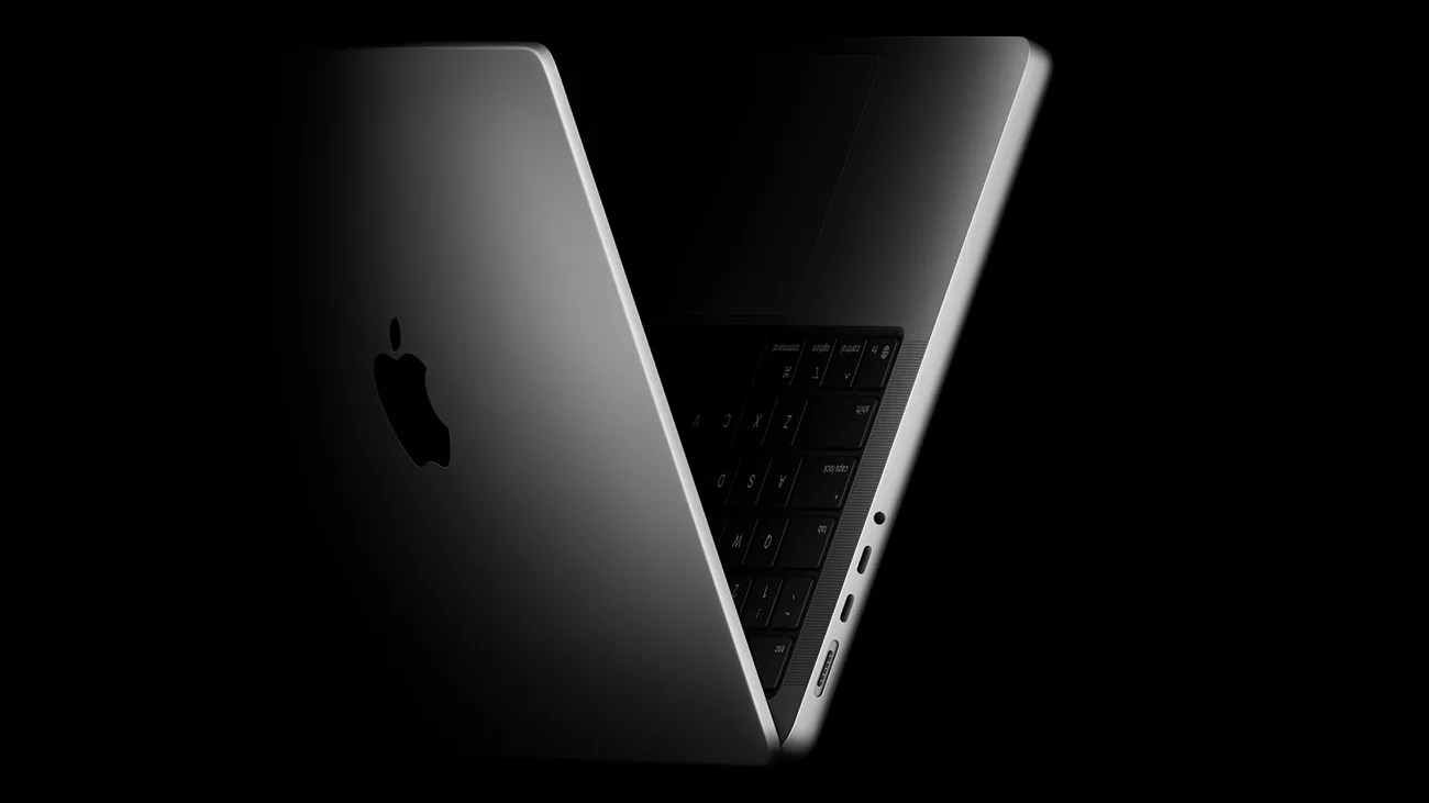 Space gray Apple MacBook partially open showing side ports and keyboard in low light on black background.