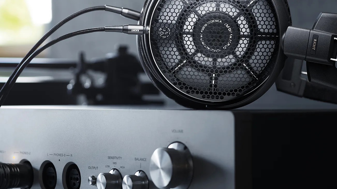 Black Audio-Technica open-back headphones connected to a silver audio amplifier with knobs.