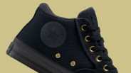 Black high-top sneaker with gold eyelets and a fuzzy inner lining against a beige background.