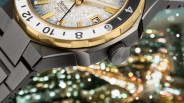 Close-up of a stainless steel watch with a gold bezel, textured silver dial, and black-and-white GMT bezel.