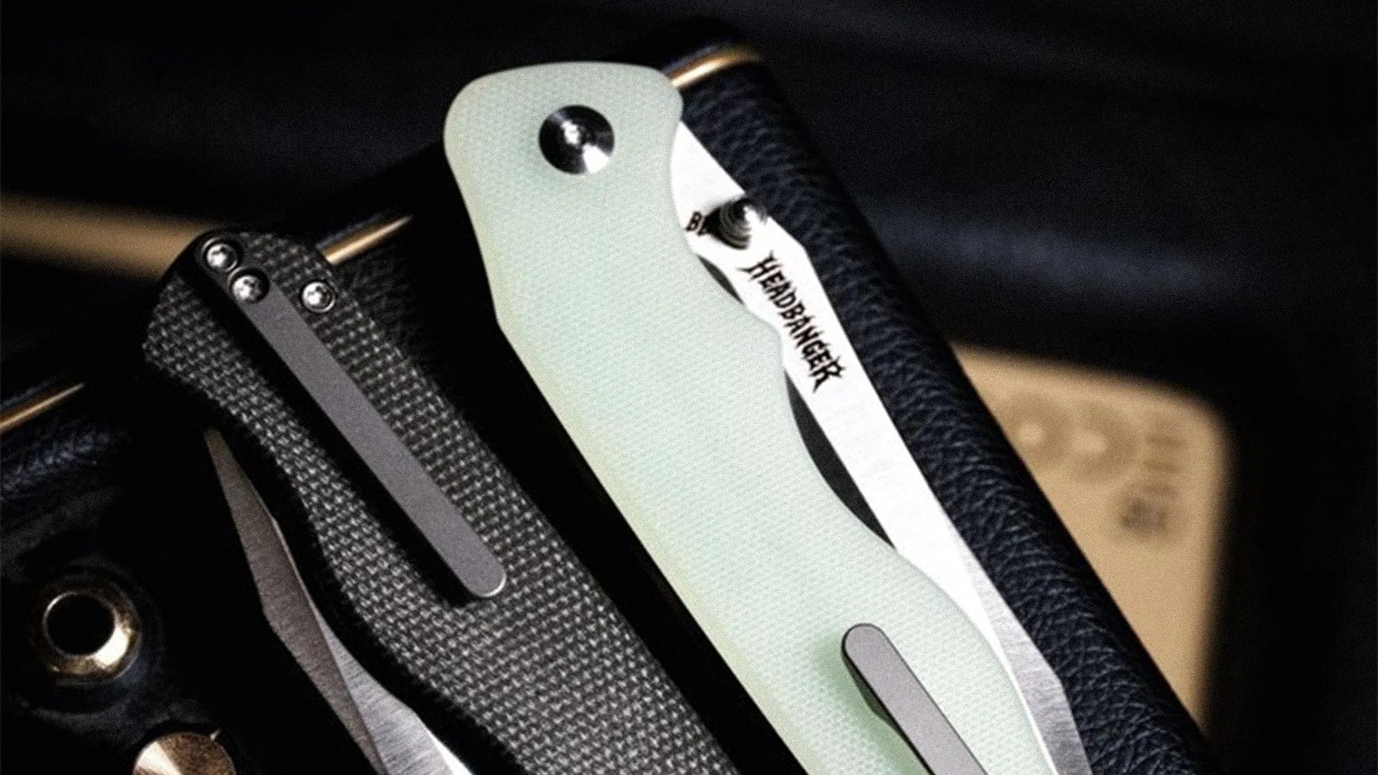 Two folding knives with pocket clips, one with a textured black handle and the other with a smooth light green handle.