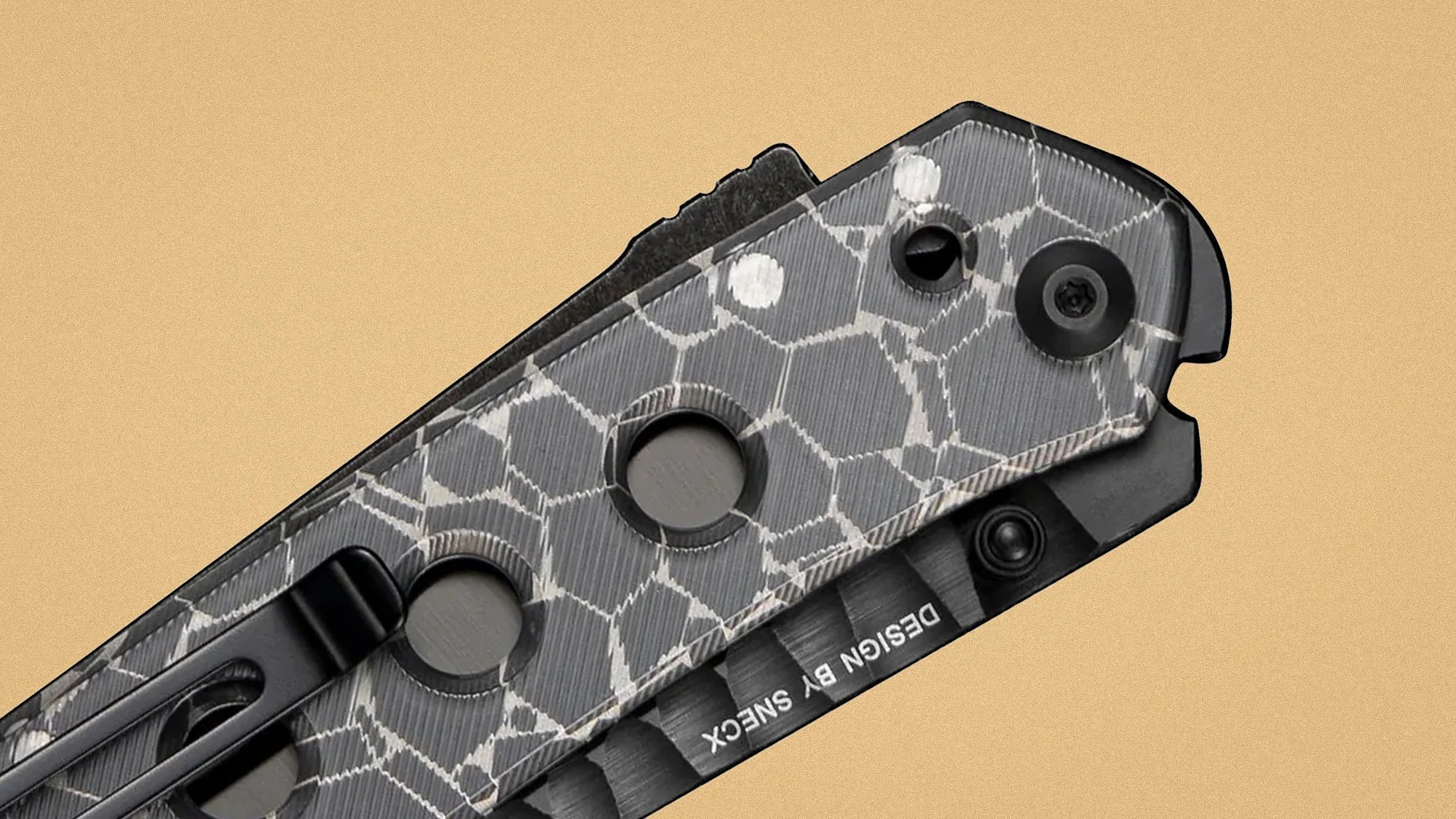 Close-up of a folding knife handle with a gray and white cracked pattern, black clip, and "DESIGN BY SNECX" text.