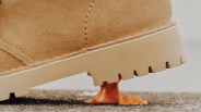 Close-up of a tan suede boot sole stuck in orange chewing gum on asphalt.