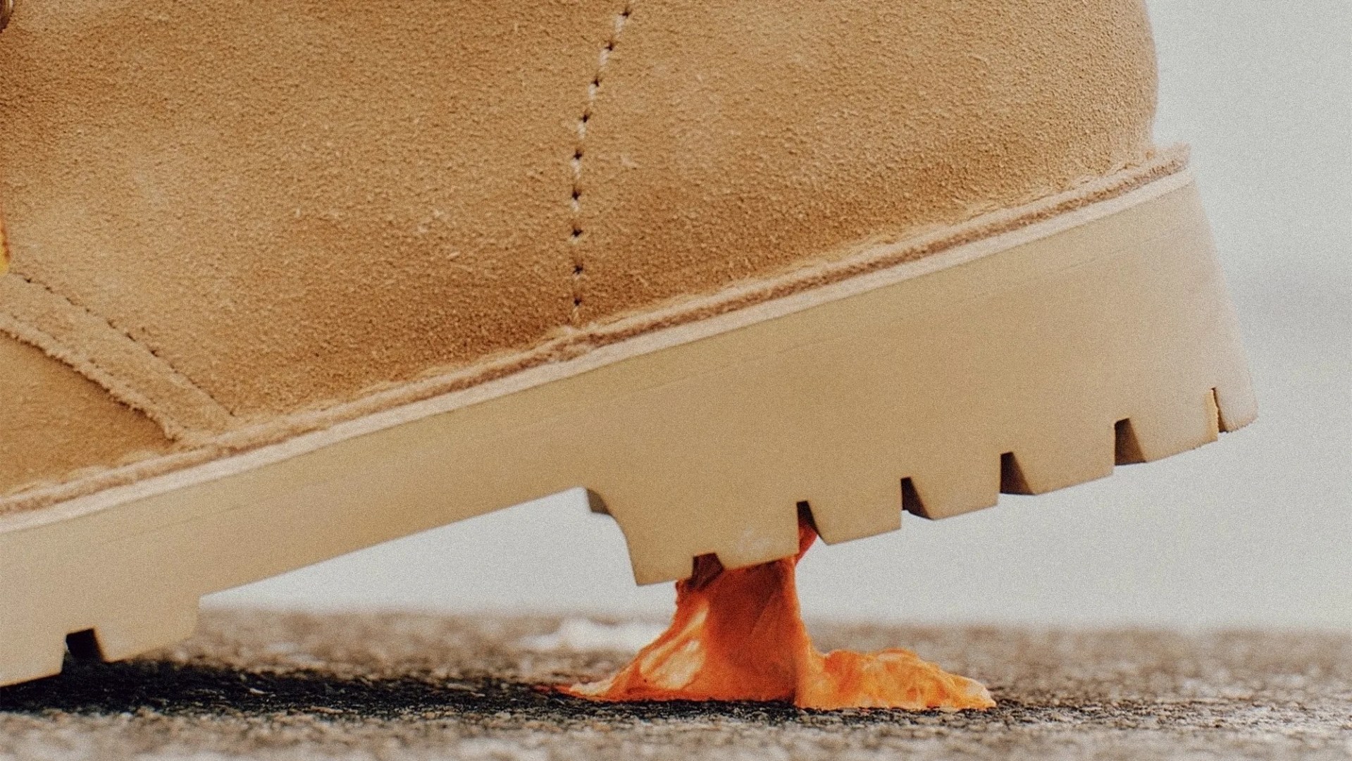 Close-up of a tan suede boot sole stuck in orange chewing gum on asphalt.