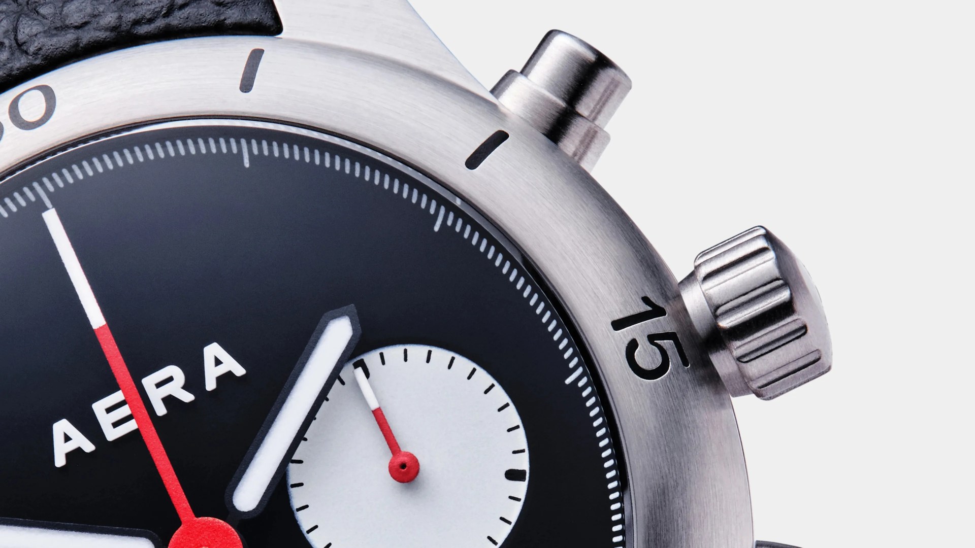 Close-up of a black and white AERA watch face with red and white hands and a stainless steel bezel marked with 15.