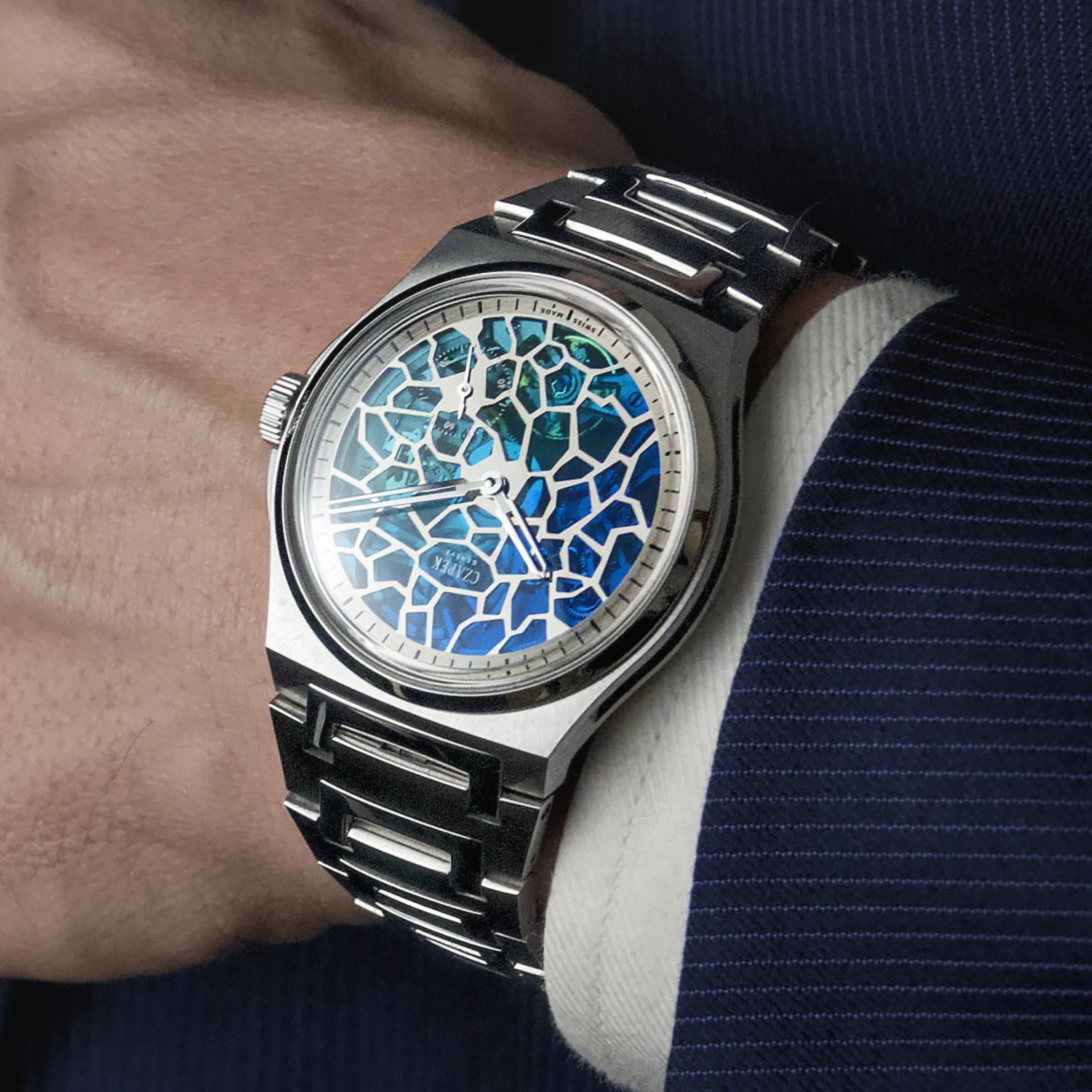 Silver wristwatch with a blue mosaic-patterned dial and a stainless steel bracelet worn on a wrist.
