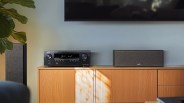 Black Denon audio receiver and gray Polk center speaker on a wooden media console under a wall-mounted TV.
