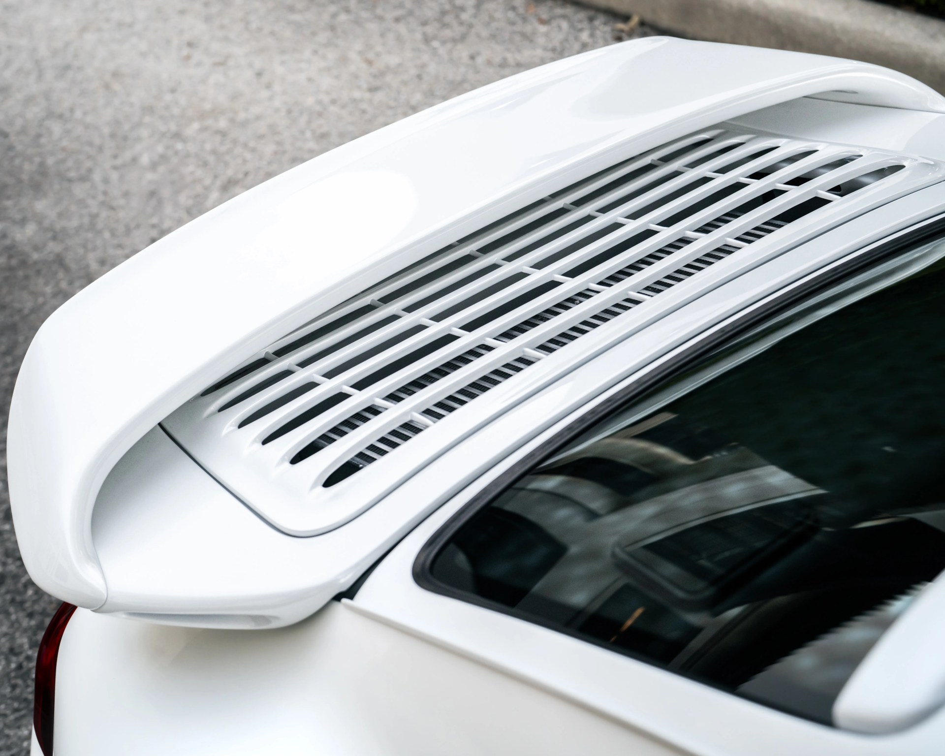 White rear spoiler and vented engine cover on a white sports car.