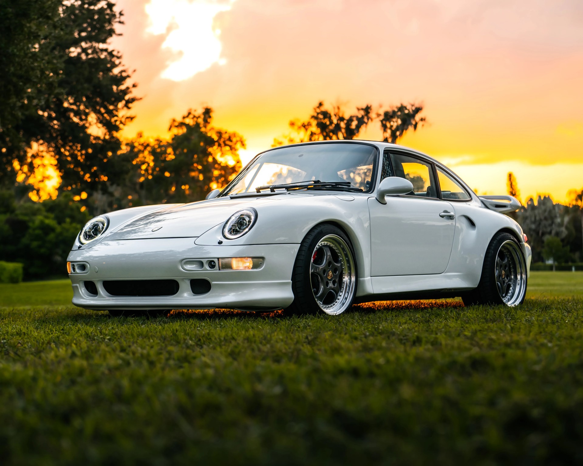 White classic Porsche sports car with black rims parked on grass at sunset.
