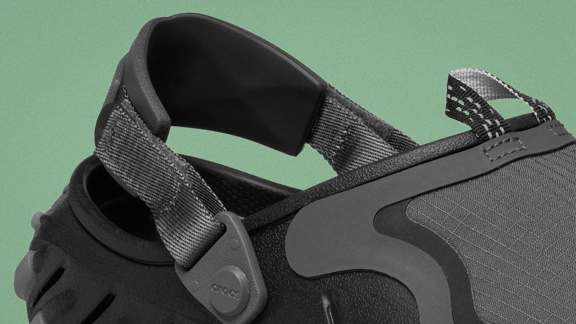Close-up of a black and gray Crocs sandal strap with textured fabric and plastic button detail.