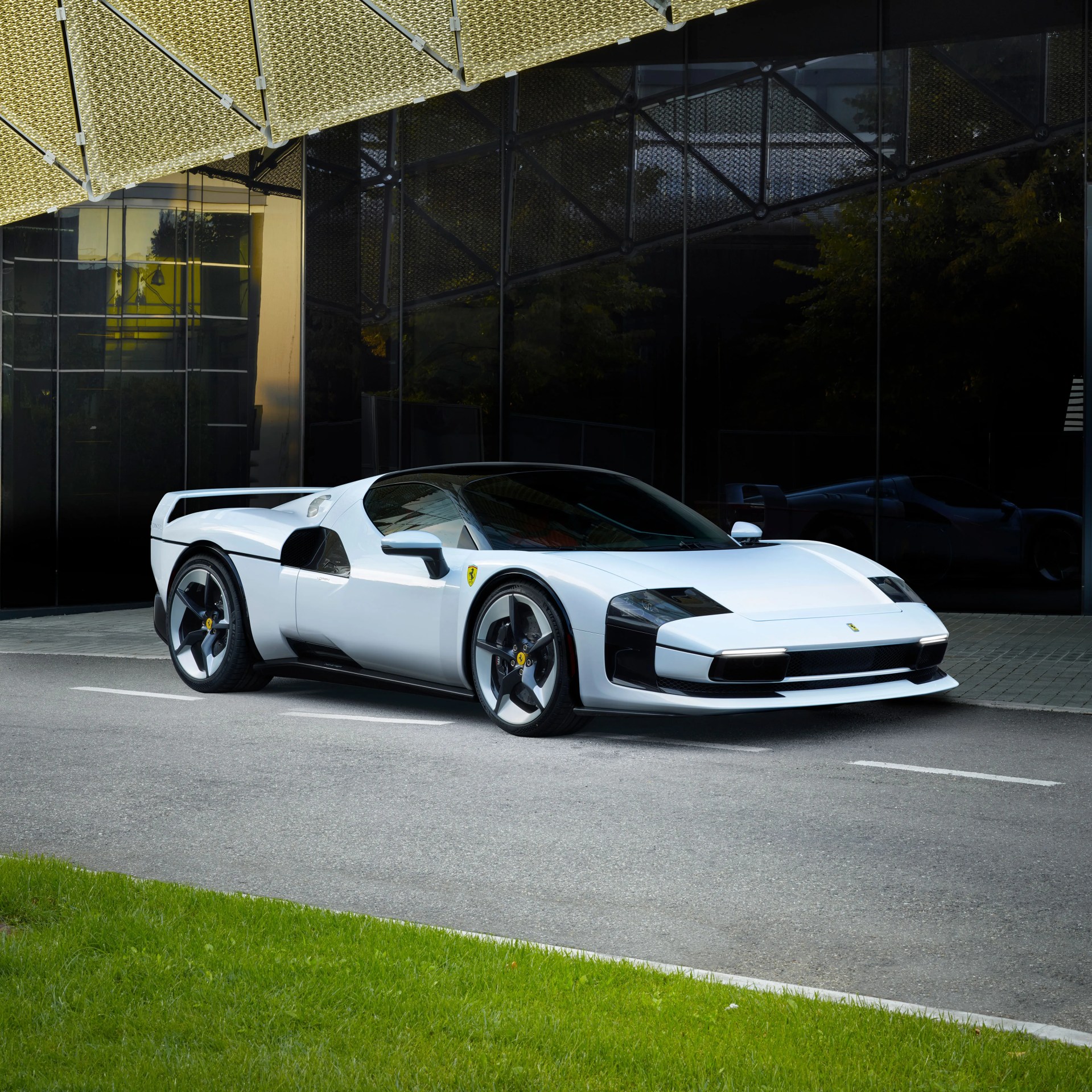 White Ferrari sports car with black accents parked on a street in front of a reflective glass building.