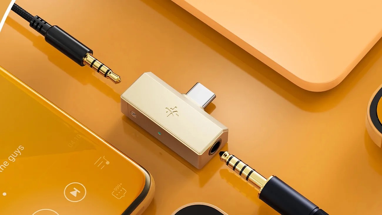 Gold-colored USB-C to 3.5mm headphone jack adapter with two black and gold audio cables on an orange surface.