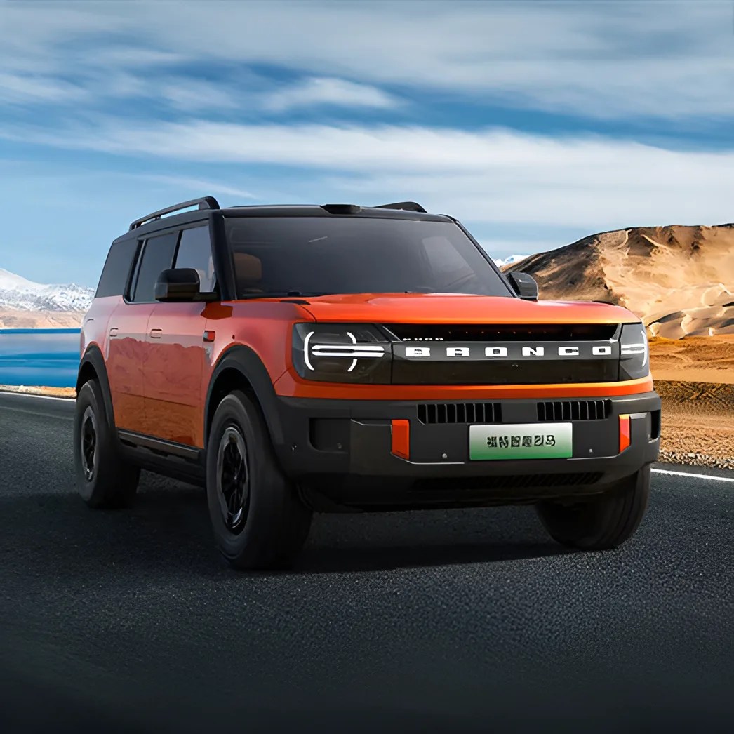 Orange Ford Bronco SUV with black roof and grille driving on a road near a lake and desert hills.