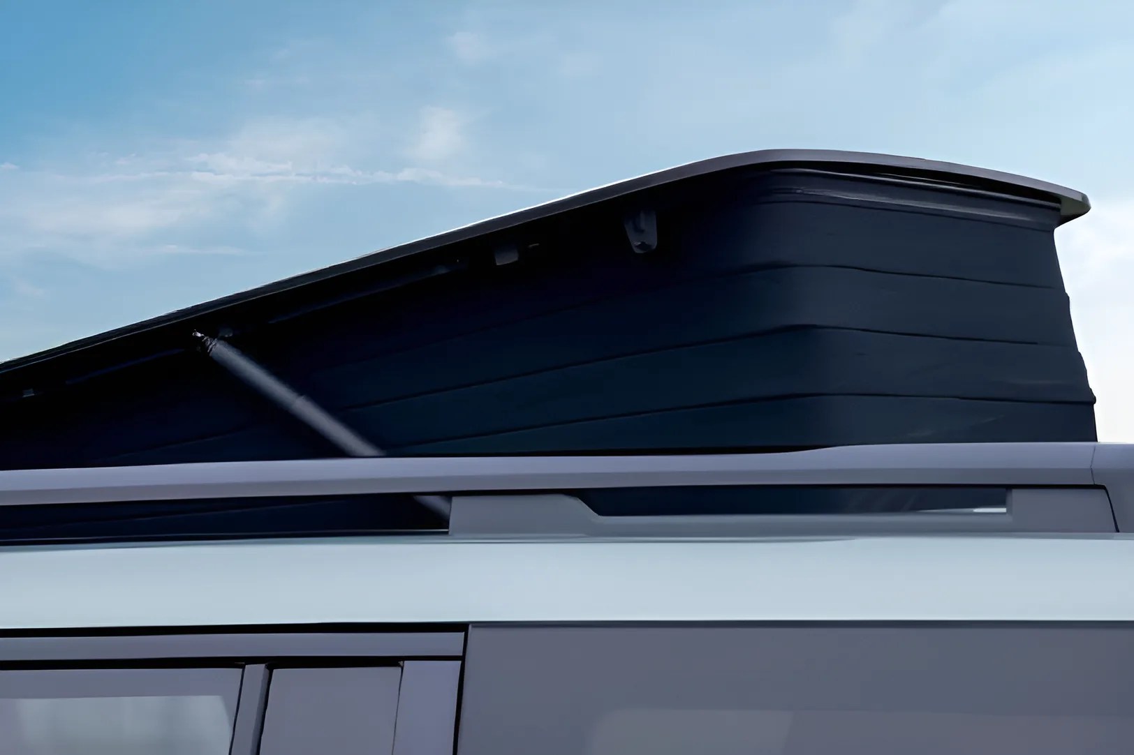 Black pop-up roof tent partially extended on a white vehicle roof against a blue sky.