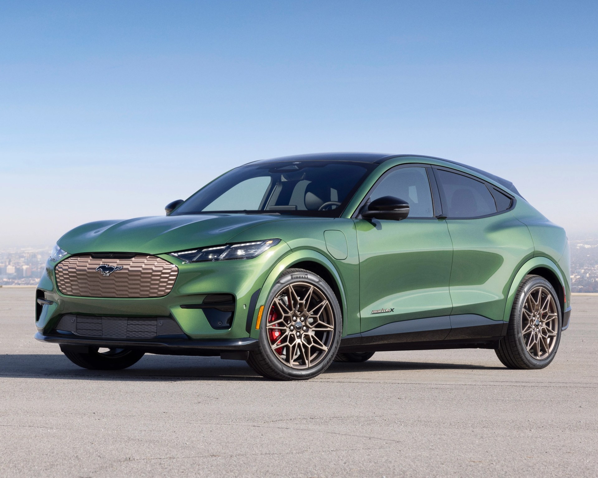 Metallic green Ford Mustang Mach-E electric SUV with bronze grille and wheels parked on concrete.