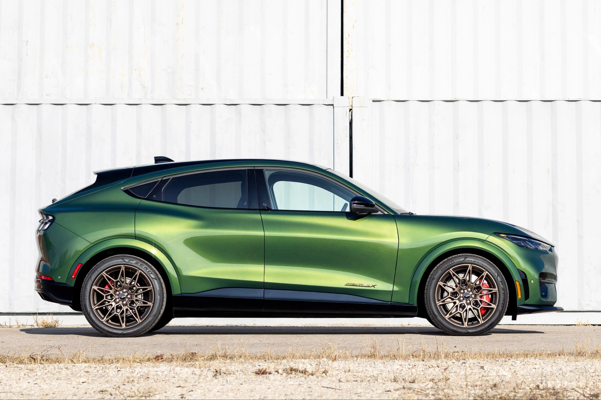 Green metallic Ford Mustang Mach-E GT with bronze multi-spoke wheels parked in front of white shipping containers.