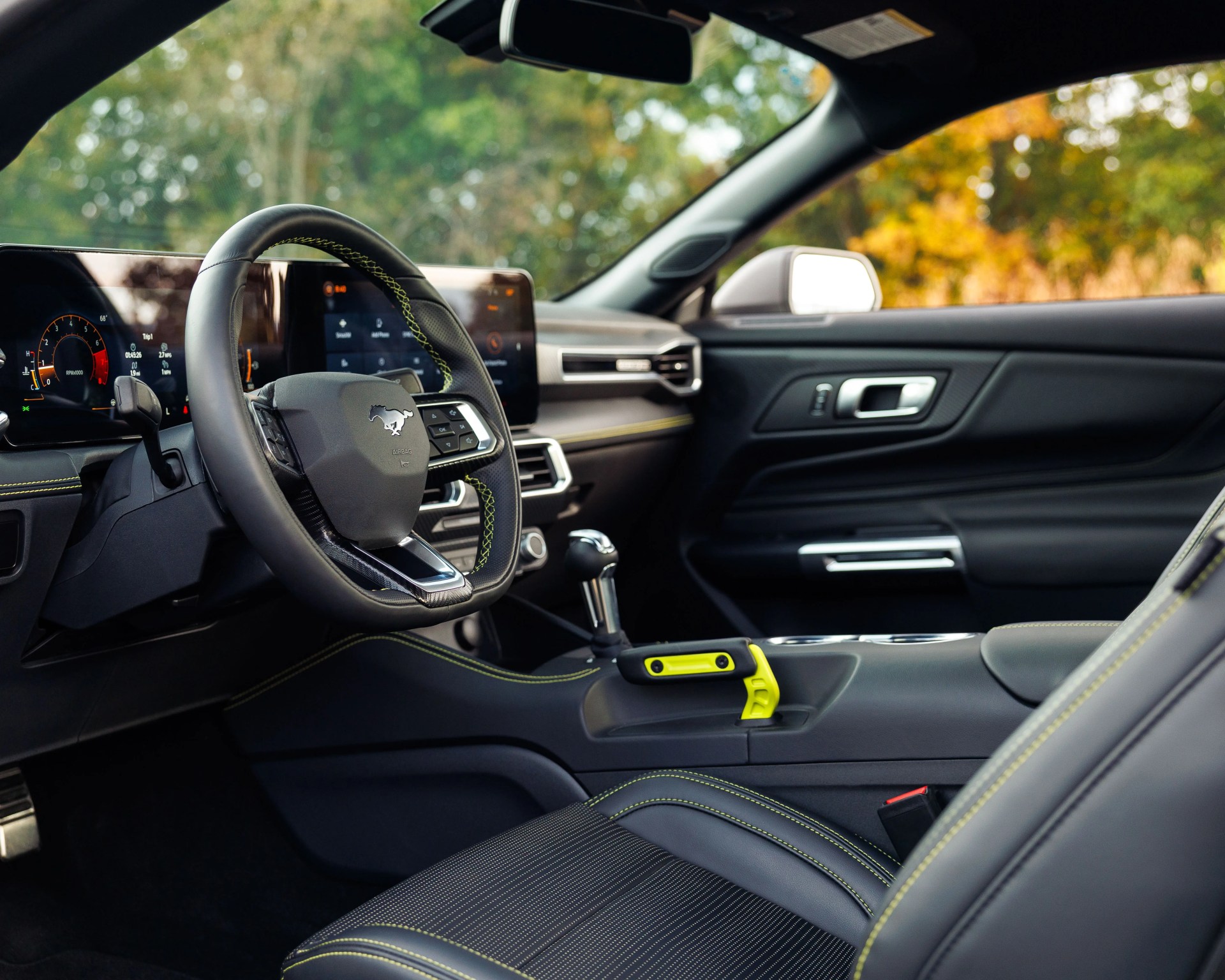 Interior of a black Ford Mustang with yellow stitching, digital dashboard, and a yellow safety tool on the center console.