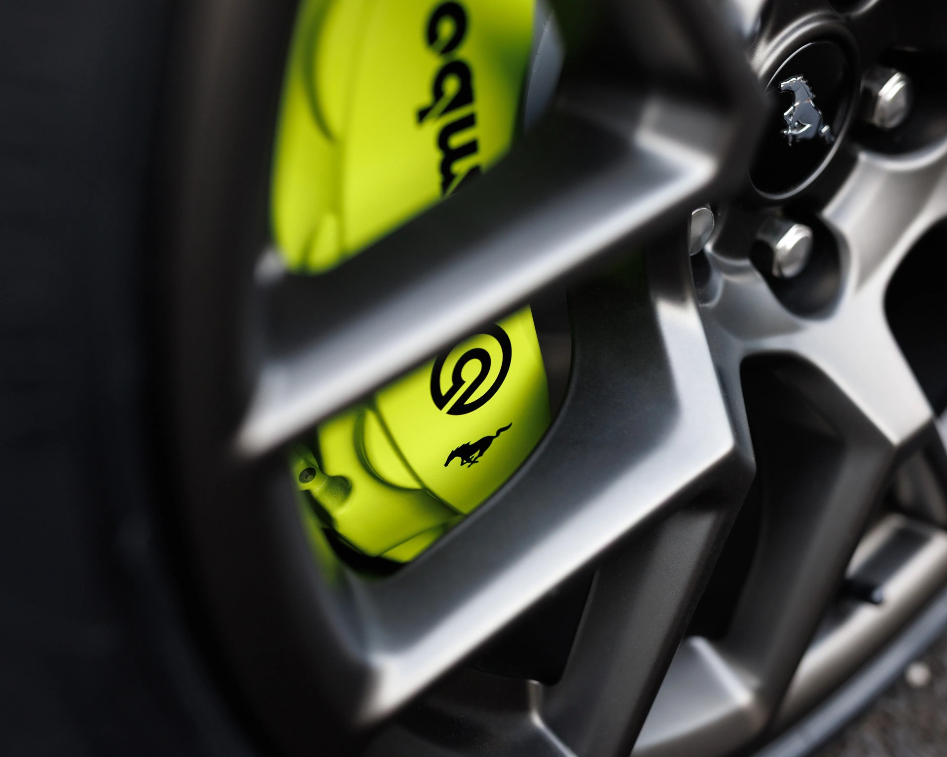 Close-up of a silver alloy wheel with a bright yellow Brembo brake caliper featuring a black Mustang logo.