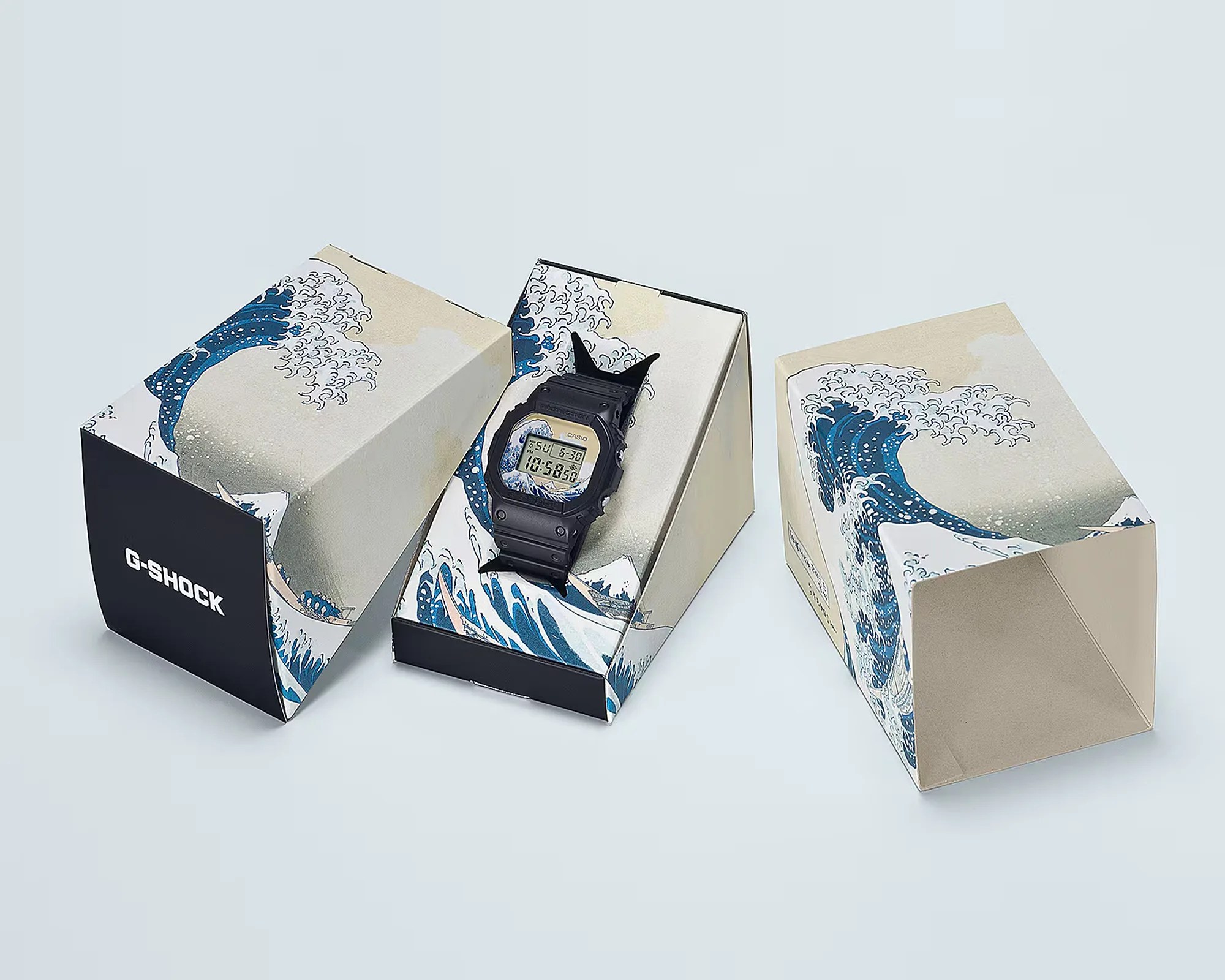 Black Casio G-Shock digital watch displayed in a box with artwork of a large blue wave and "G-SHOCK" text on the side.