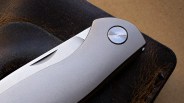 Close-up of a sleek silver folding knife with a circular pivot on a dark textured surface.