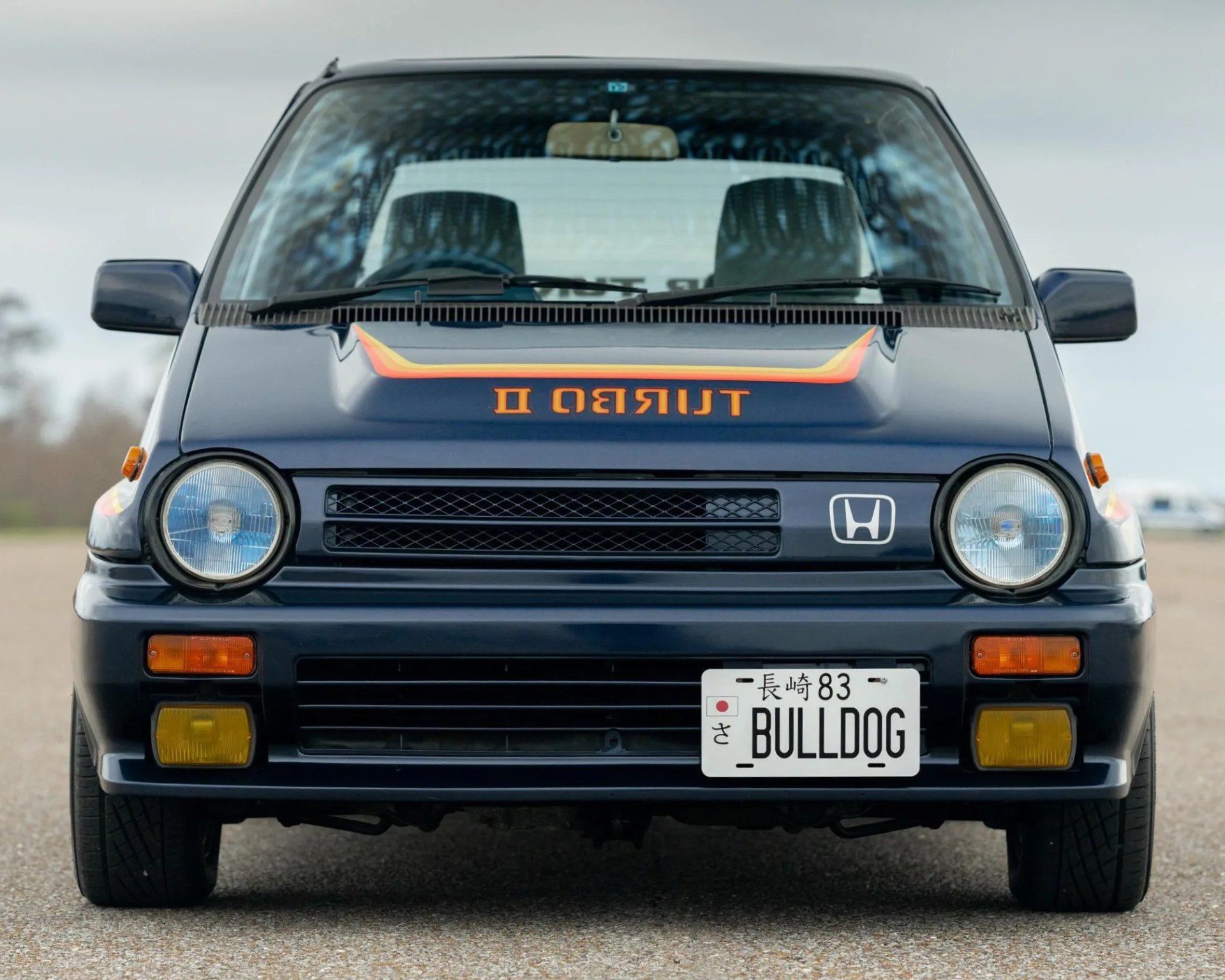 Front view of a dark blue Honda car with round headlights, "TURBO II" decal on the hood, and a Japanese license plate reading "BULLDOG.