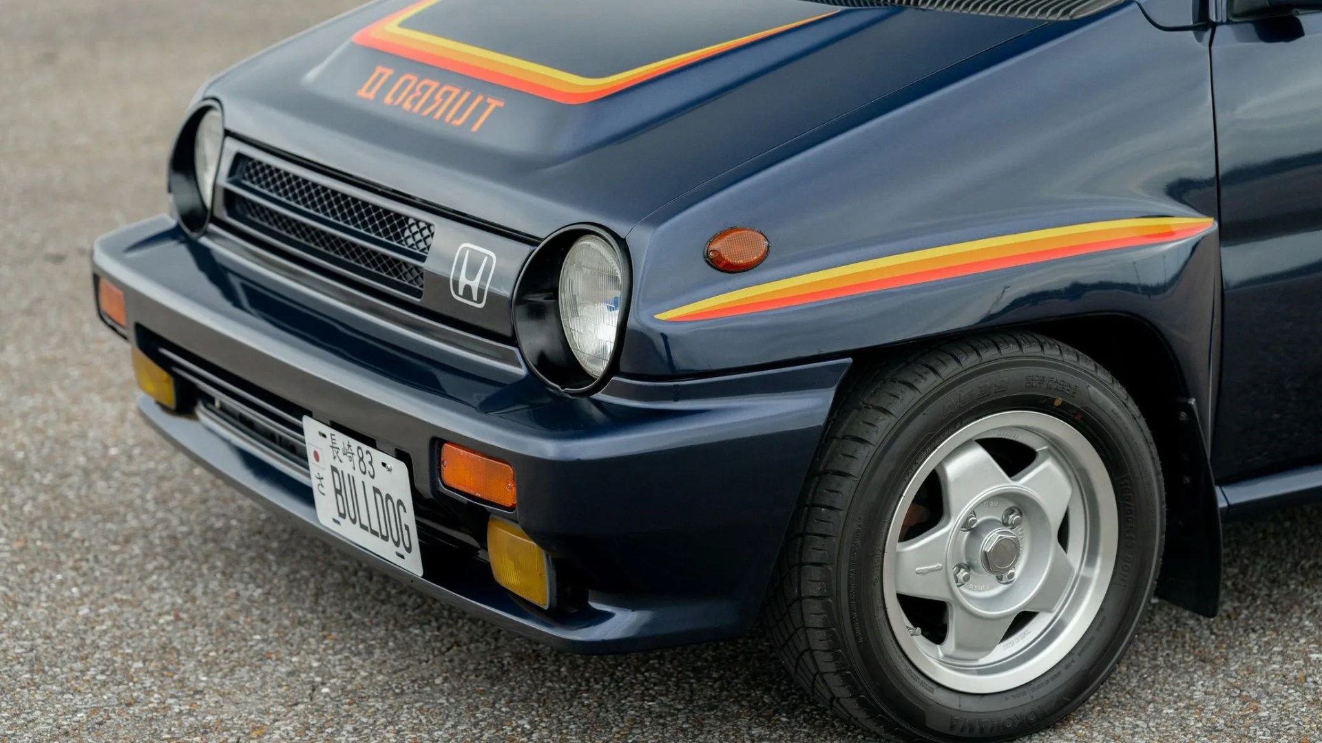 Front side of a dark blue Honda Turbo II car with yellow and red stripes and a license plate reading "BULLDOG.