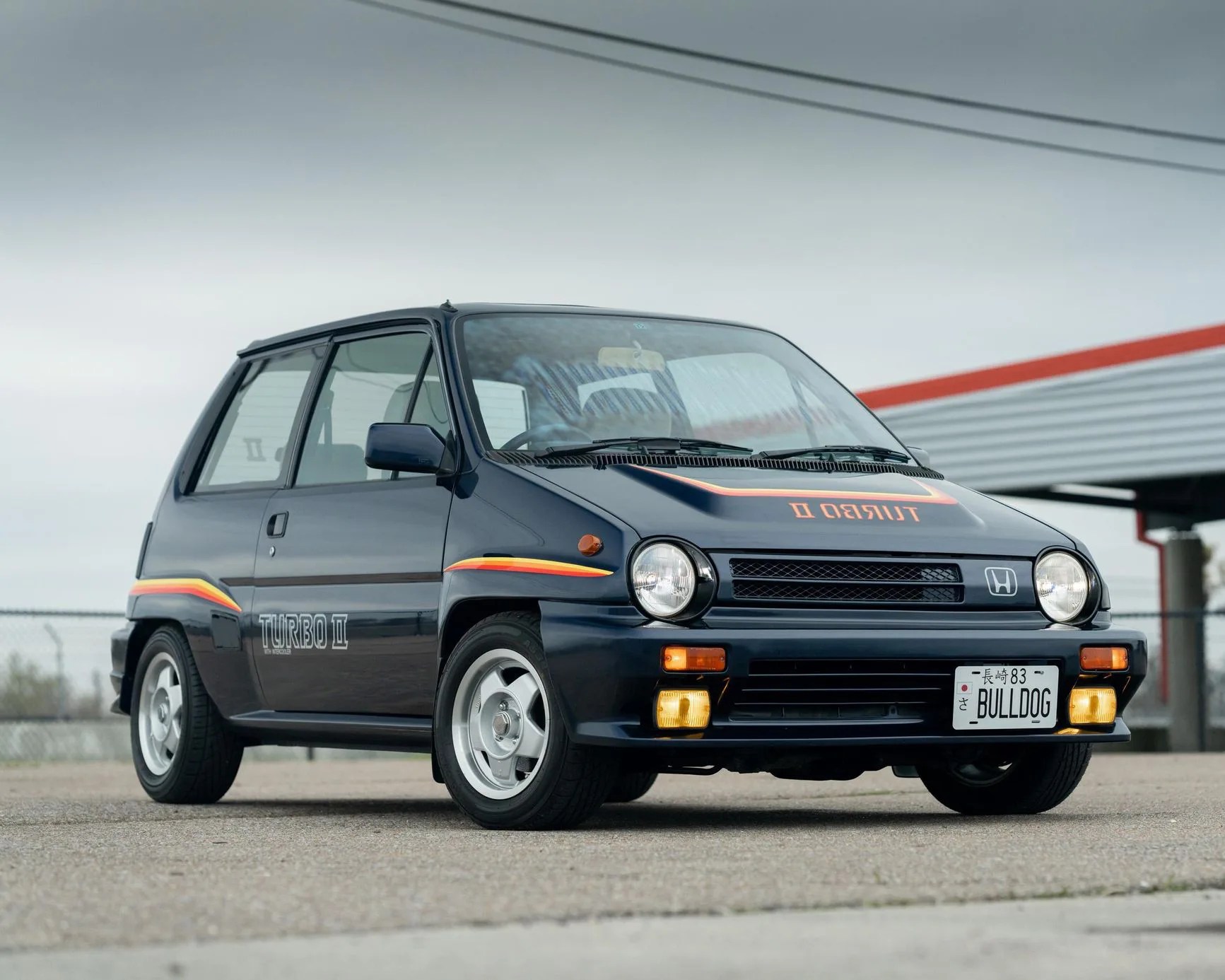 Dark blue Honda hatchback with "Turbo II" decals and Japanese license plate reading "BULLDOG" parked outdoors.