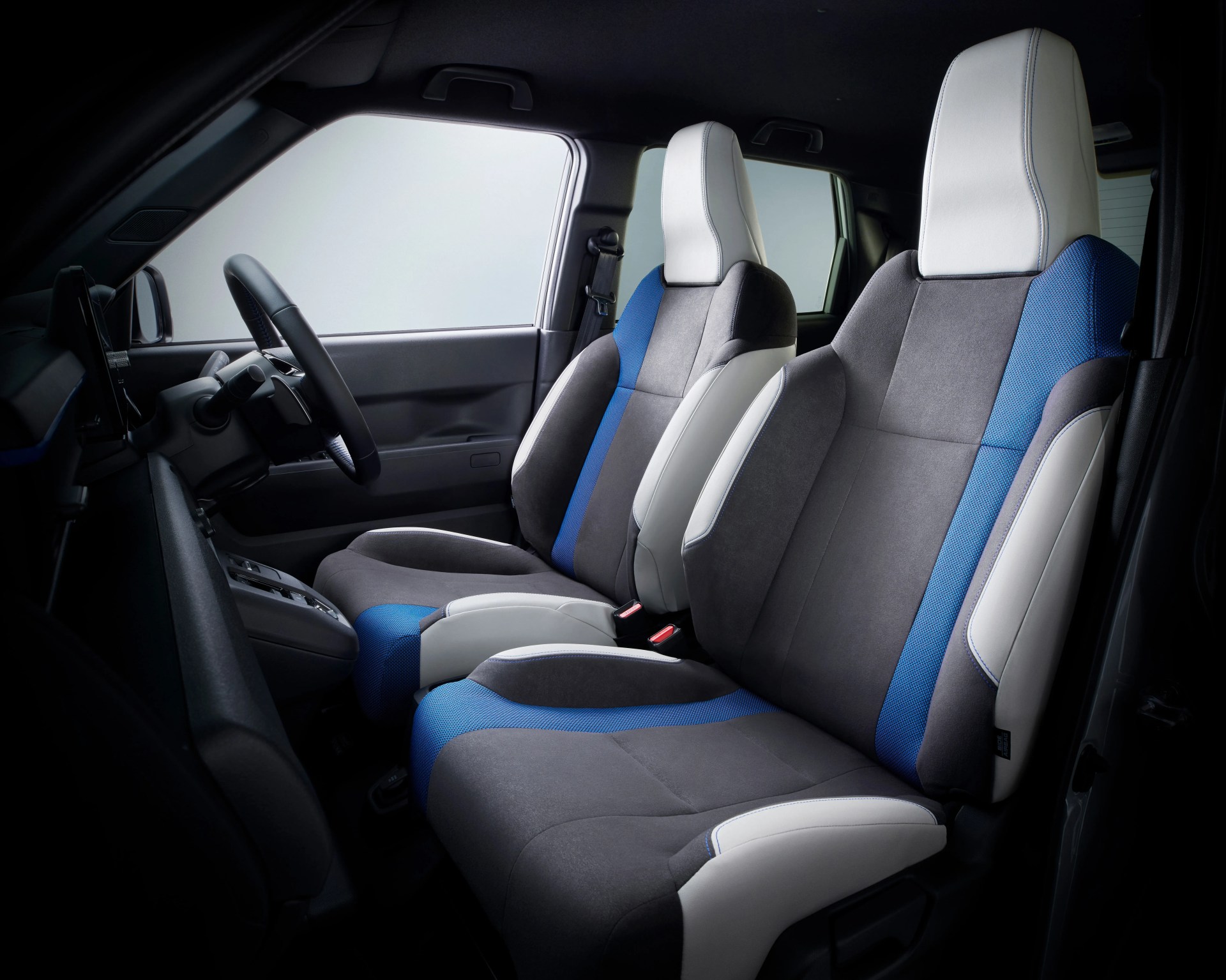 Two-tone car seats in gray, blue, and white fabric inside a vehicle cabin with a black steering wheel and dashboard.