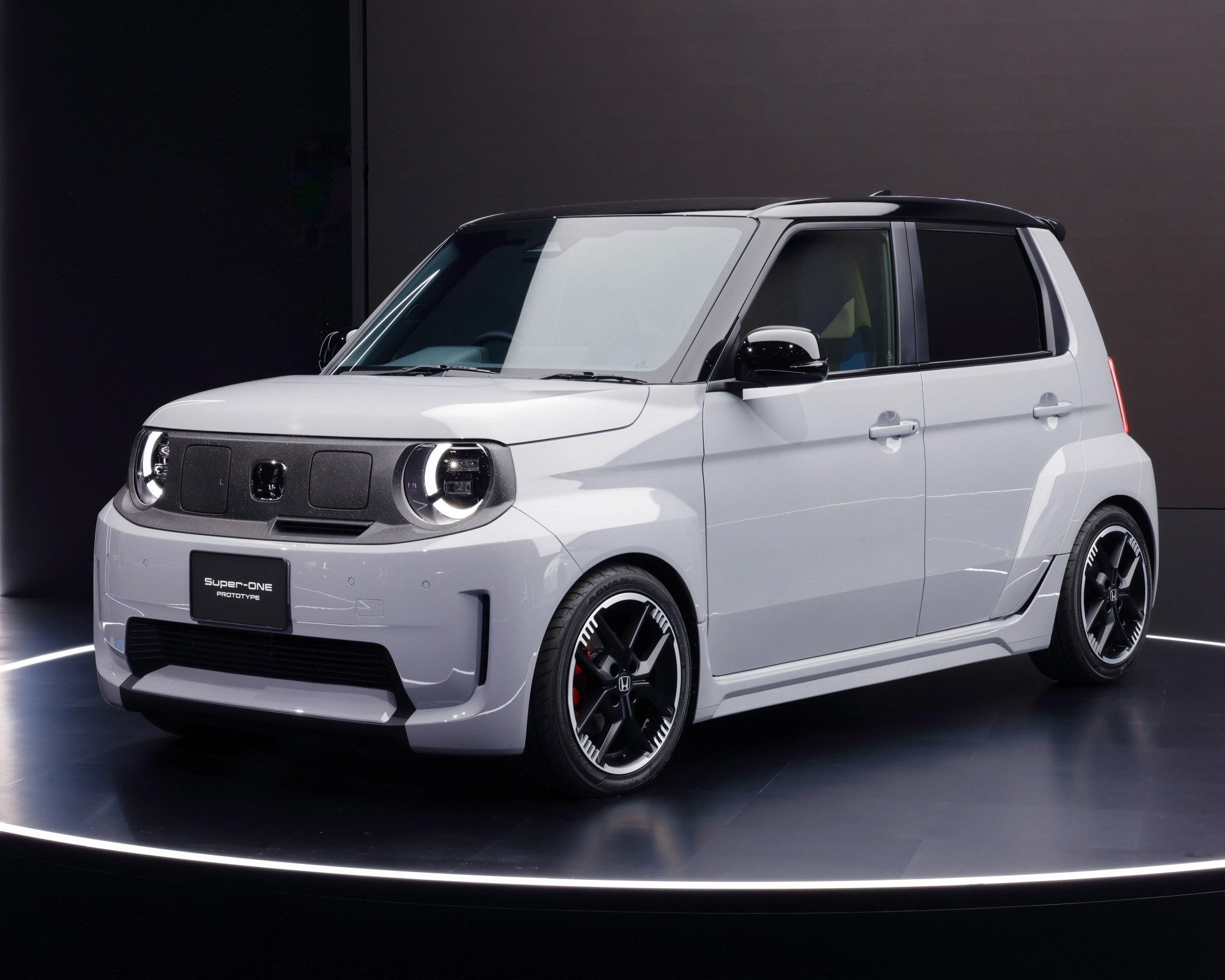 White compact Honda Super-ONE prototype car with black roof and sporty black alloy wheels on a circular platform.
