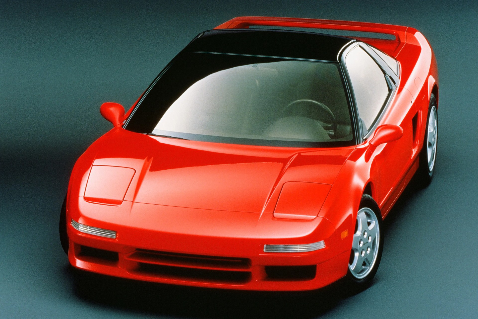 Red sports car with pop-up headlights and black roof panel viewed from front right angle.