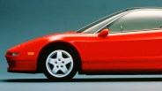 Red Acura sports car front side with silver five-spoke wheel on a gray surface and blue background.