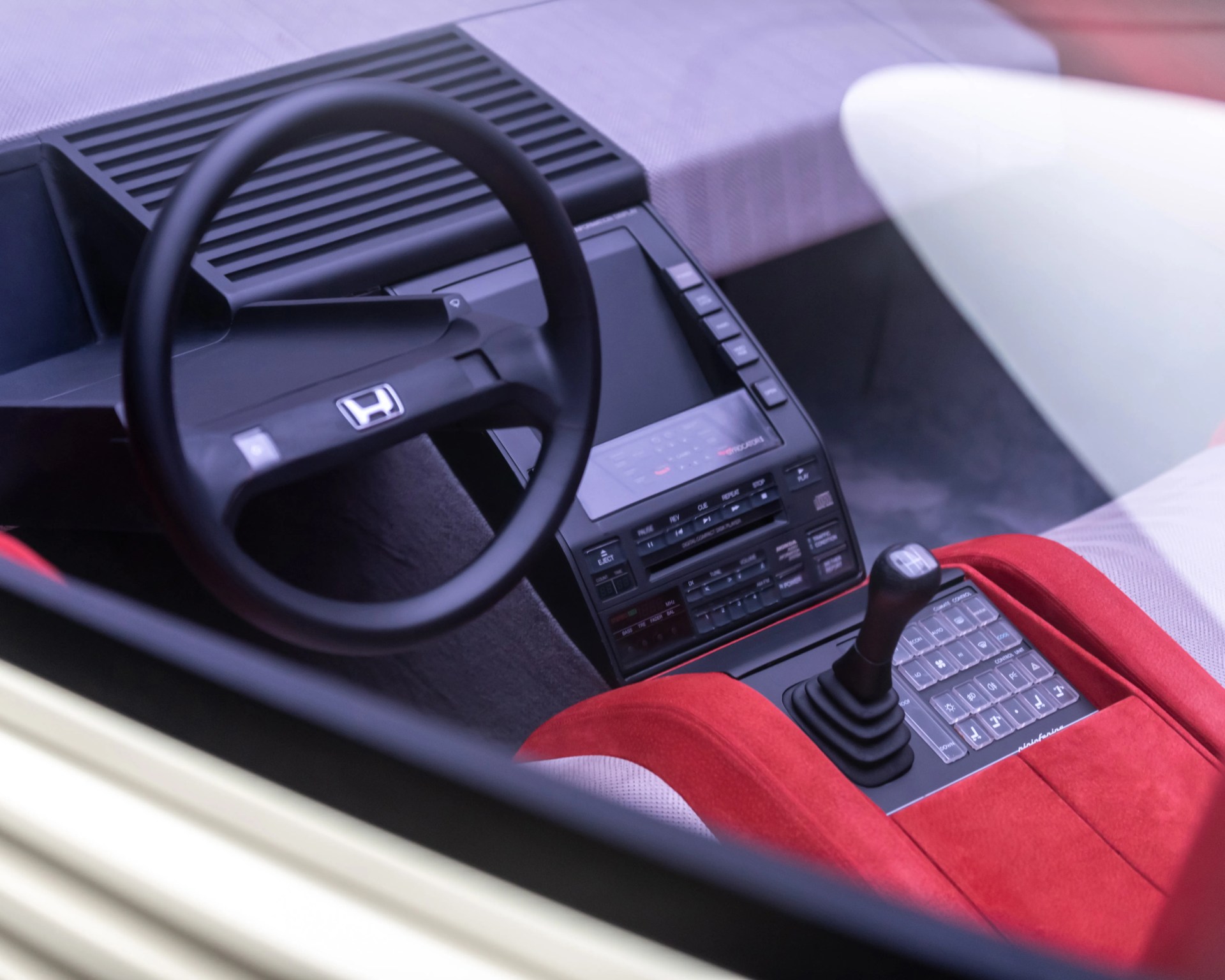 Black Honda steering wheel and gear shift lever in a car interior with red and gray seats and a digital dashboard.