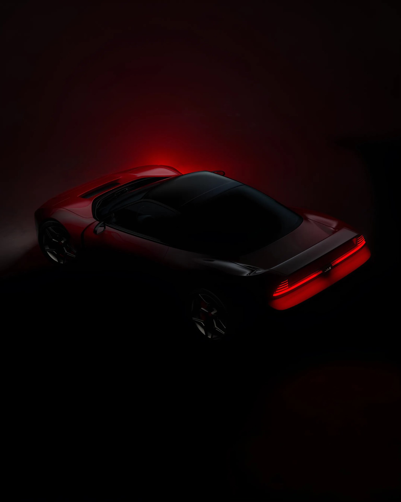 Red sports car with illuminated rear lights in a dark setting viewed from above.