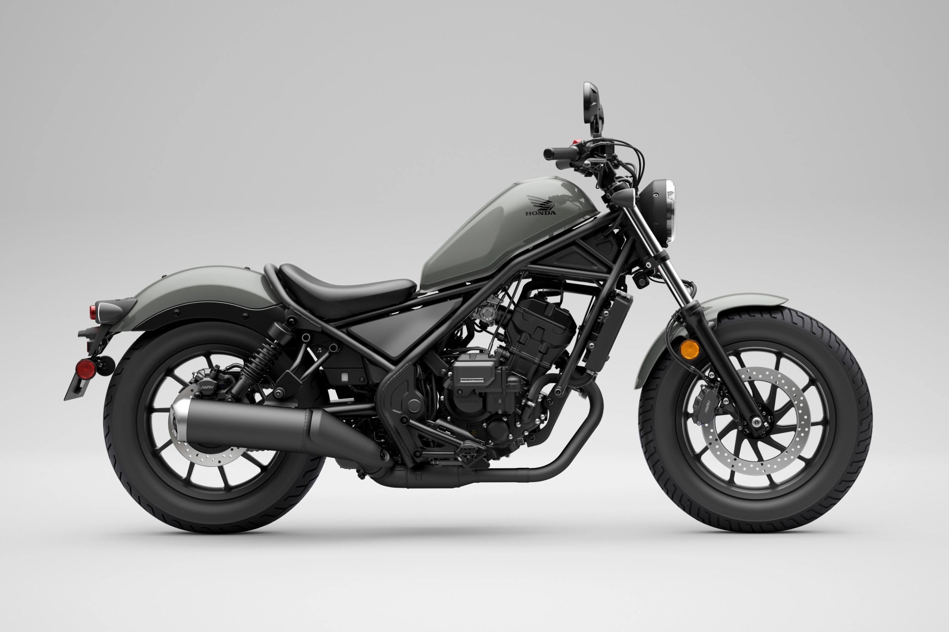 Matte gray Honda motorcycle with black frame, single seat, and round headlight on a gray background.
