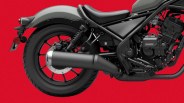 Rear section of a black motorcycle showing the rear wheel, exhaust pipe, suspension, and part of the engine against a red background.