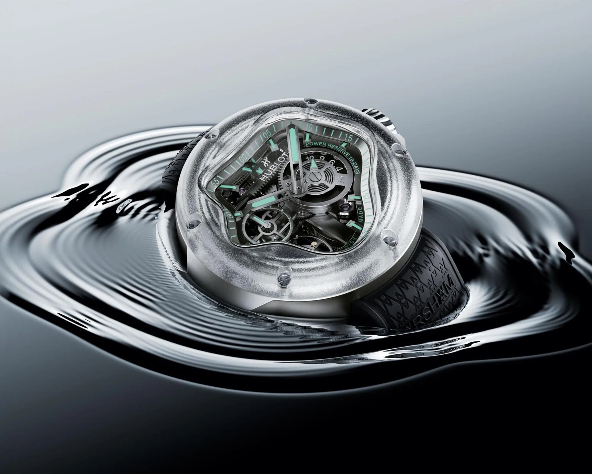 Silver and transparent Hublot wristwatch with black rubber strap floating on rippled water surface.