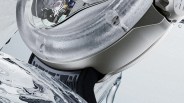 Close-up of a silver wristwatch with a textured frosted bezel, visible mechanical movement, and a black strap.