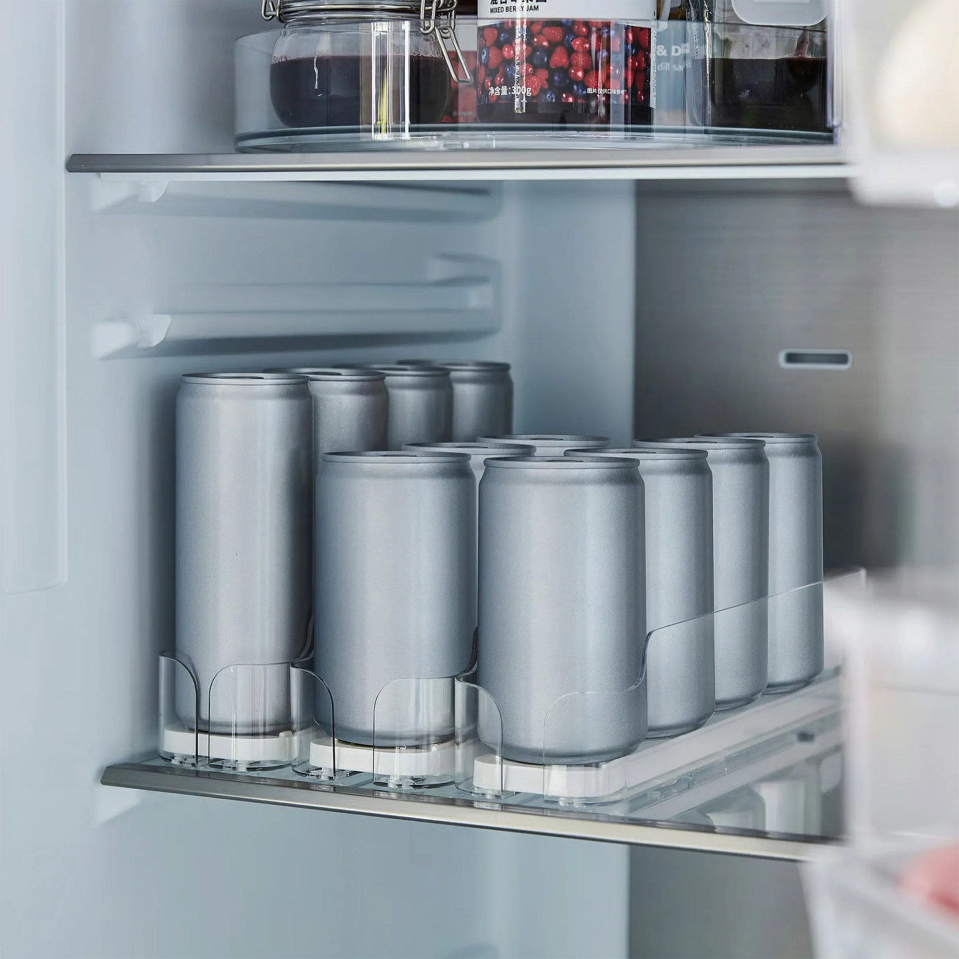 Clear plastic can organizer holding two rows of silver cans inside a refrigerator.