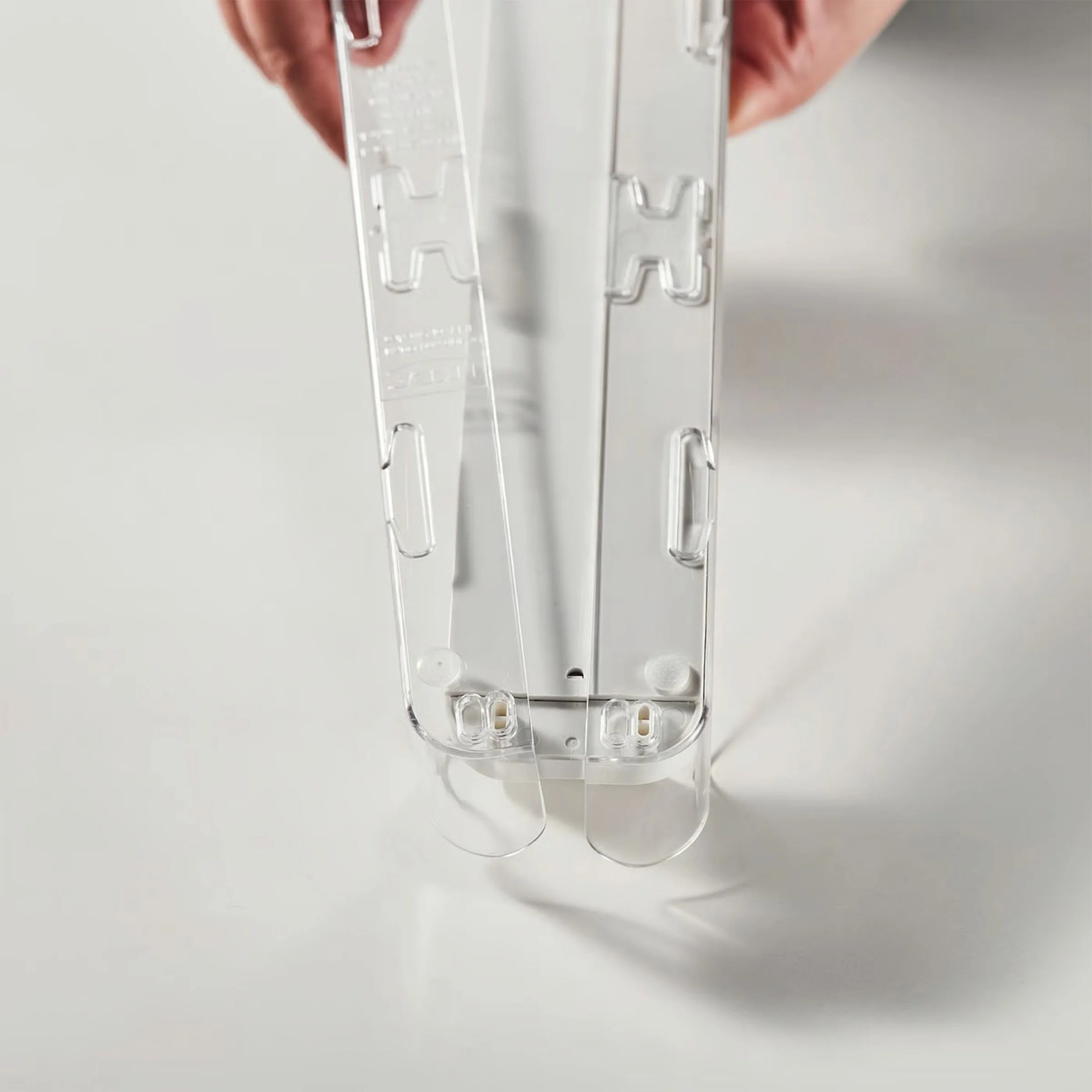 Two clear plastic stapler bases held side by side on a white surface.