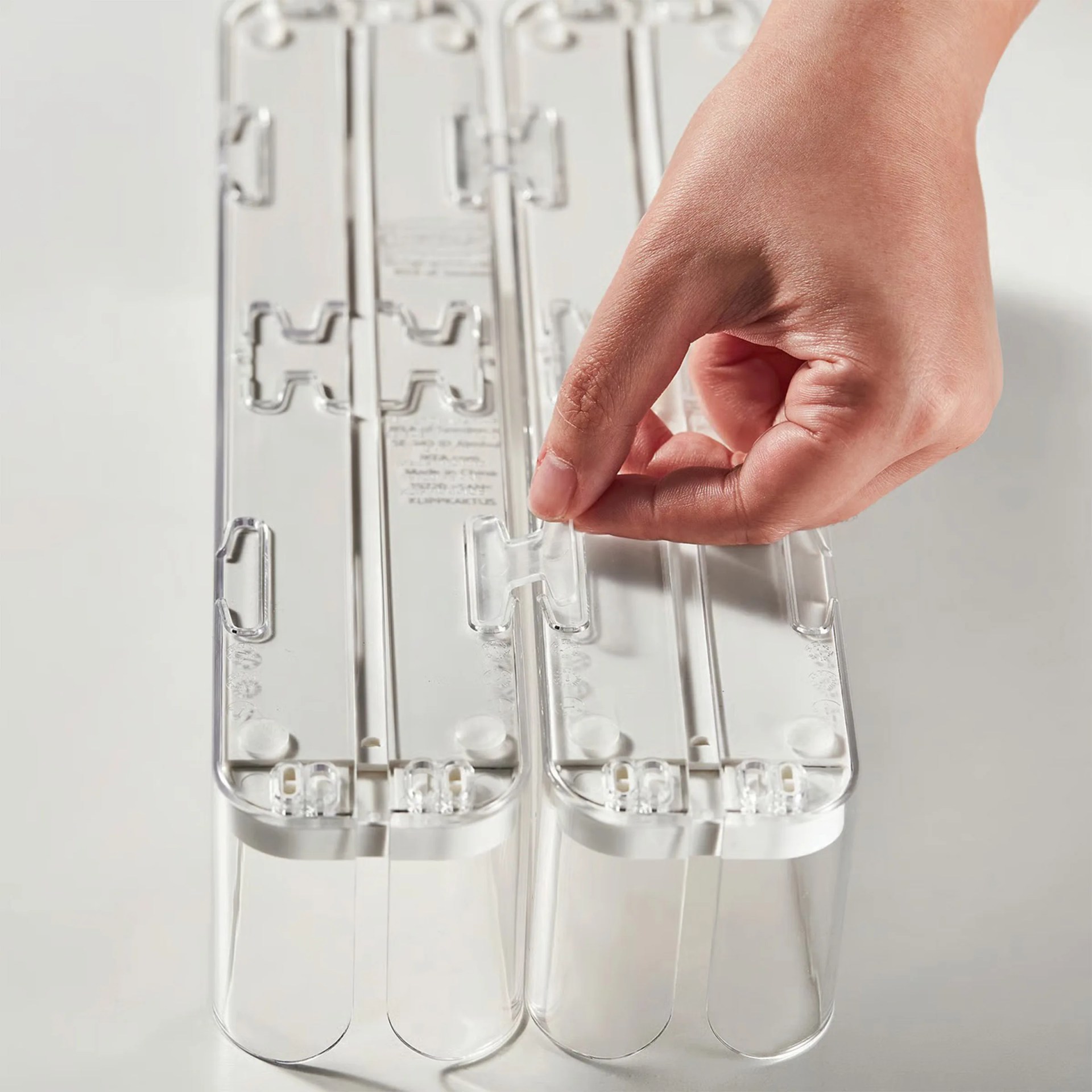 Hand lifting a clear plastic latch on a transparent rectangular container with two compartments.