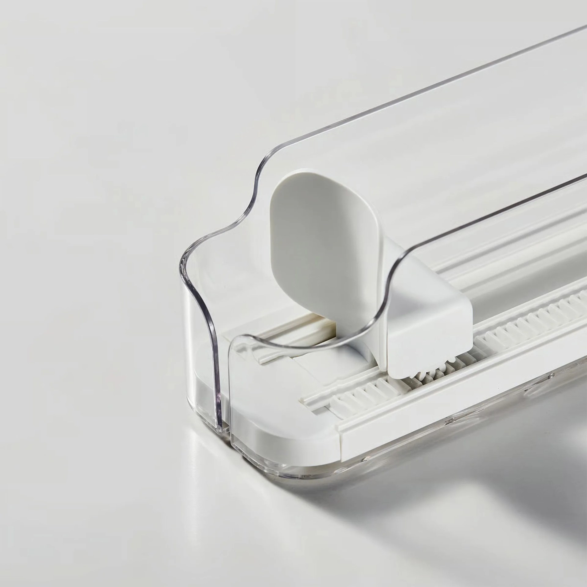 White and clear plastic adjustable paper trimmer with a sliding blade on a white surface.