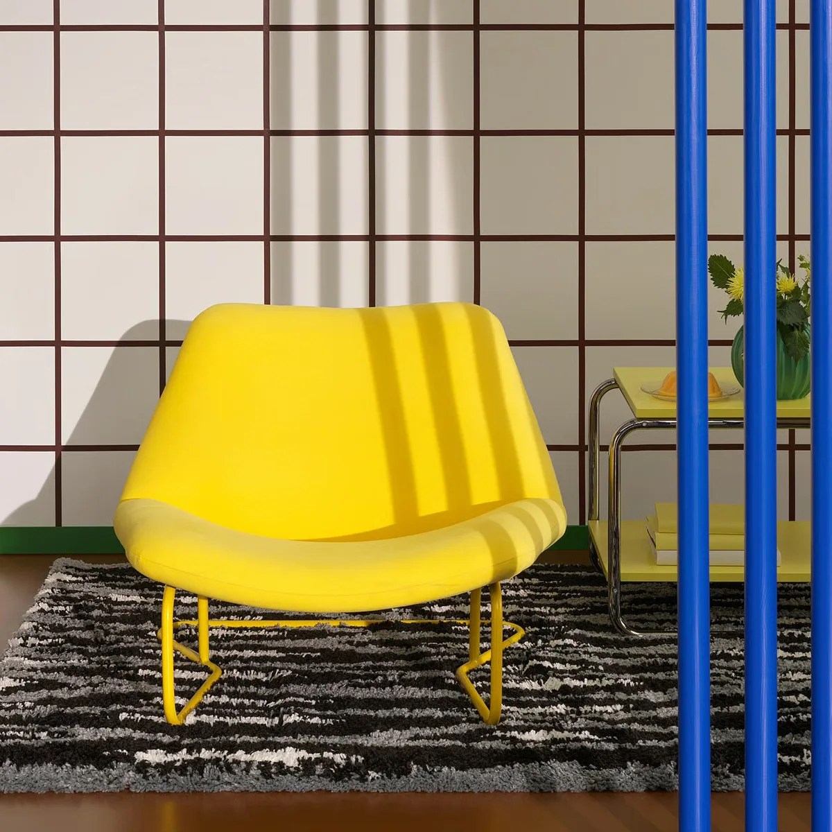 Bright yellow modern lounge chair with metal legs on a black and white patterned rug.