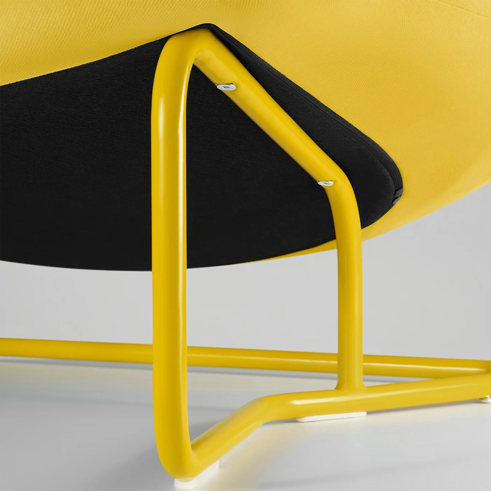 Close-up of a yellow metal chair leg with a black fabric seat underside on a white surface.