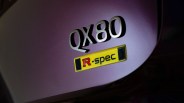 Close-up of a silver "QX80" badge and a yellow "R-spec" emblem on a purple vehicle surface.