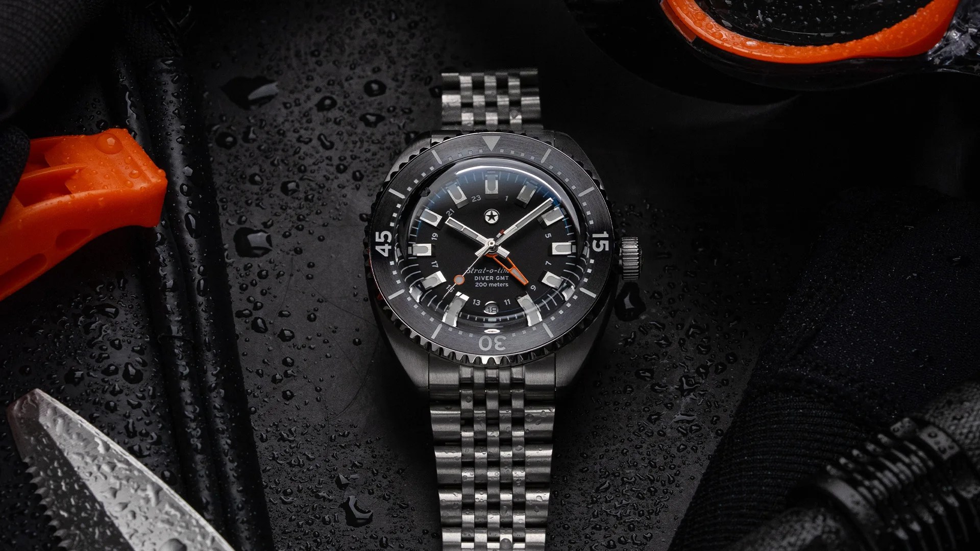 Black dial diver GMT watch with stainless steel bracelet and orange GMT hand on a wet surface.