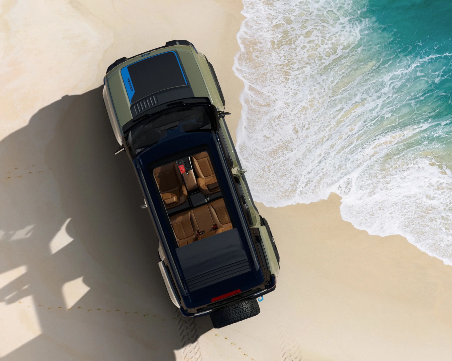 Top-down view of a green 4x4 vehicle with tan leather seats parked on sandy beach near ocean waves.