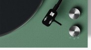 Close-up of a green turntable with black tonearm and two silver control knobs.